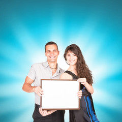 Young couple in love. Handsome guy and pretty girl with pose on blue background in studio. They wear T-shirts, trousers, dress & hold isolate white frames in hands