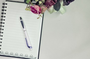 Top or flat lay view of eyeglass and notebook with flower decoration on white table background with copy space.