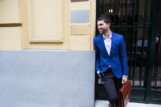 Young man wearing elegant suit holding brief case and laughing smiling away at street. 