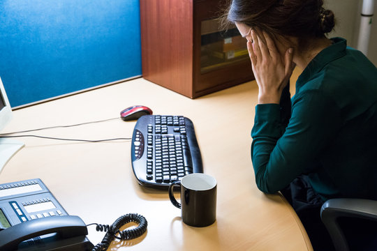 Young businesswoman sitting at desktop with computer and looking tired holding hands on temples. 