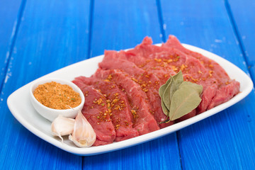 raw meat with herbs on white dish on blue wooden background