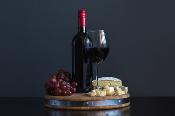 Bottle and glass with red wine near cheese composition on a wooden board