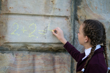 Girl with pigtails, wrote a mathematical example on a stone wall. schoolgirl