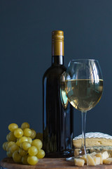 Obraz premium Bottle and glass with white wine near cheese composition on a wooden board
