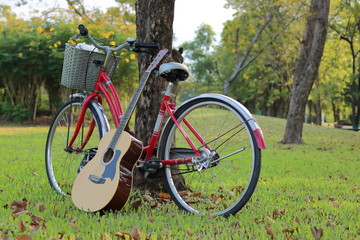 Fototapeta premium Acoustic guitar leaning a red bicycle in nature summer park.