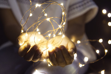 Woman hands holding string of lights in the dark to make a wish.
