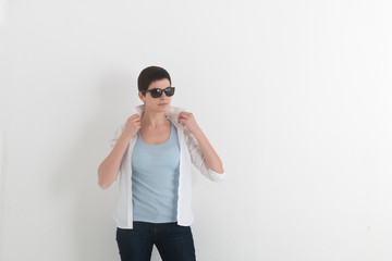 Portrait of young girl in jeans and sunglasses with short hair holding a white shirt collar