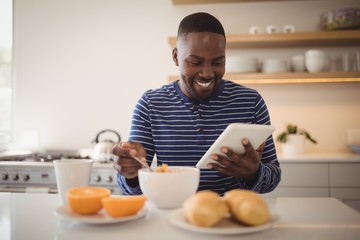 Fototapeta na wymiar Smiling man using a digital tablet while having breakfast in kit