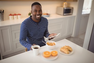Smiling man using a digital tablet while having breakfast in kit
