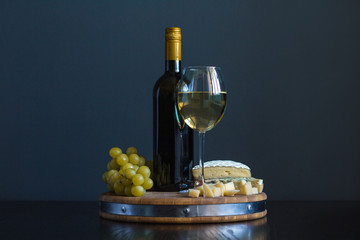 Bottle and glass with white wine near cheese composition on a wooden board