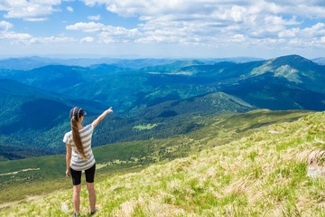 Fototapeta na wymiar Hiking girl at the peak of the mountain points to something. Enjoy the mountain view