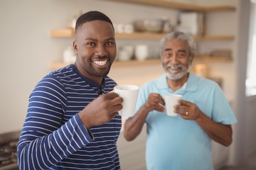 Smiling father and son having cup of coffee in kitchen