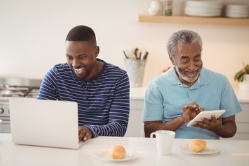Father and son using laptop and digital tablet in kitchen