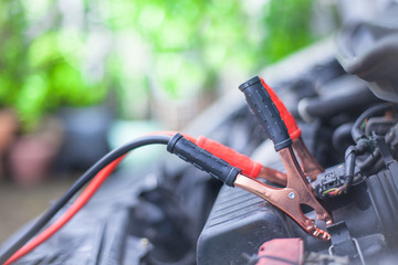 Charging car battery with electricity trough jumper cables with copper clamps attached for start...