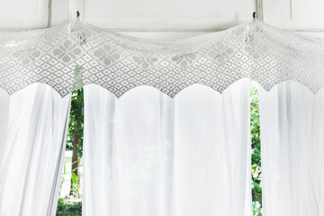 White curtains with patterns on veranda of residential wooden house. Balcony in rustic style, sunlight from window