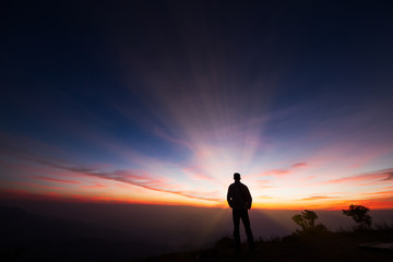 Silhouette of a man standing on the cliff looking at sunrise background, hope and following a dream...