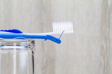 Interdental brush, toothbrush and dental floss on clean glass on blurred wooden background in...