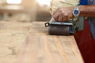 Front view of belt sander working on a piece wood with hands of worker with copy space. Selective...