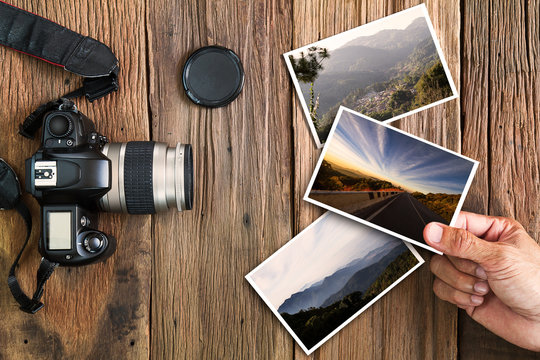 Man's hand holding photo with old grunge camera and photos on vintage grunge wooden background, vocation photography concept