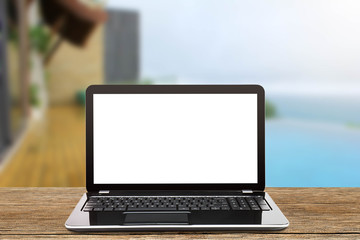 Laptop with blank white screen on vintage wooden table on blurred pool and beach background