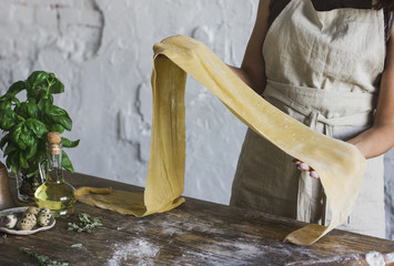 Young woman in apron holding a dough for homemade pasta at rustic kitchen