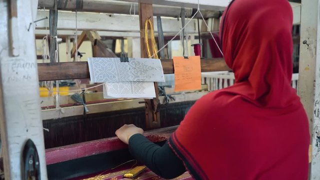 Medium shot of Indonesian woman weaving fabric with foot-treadle loom machine. Shot with Sony a7s and Atomos Ninja Flame in Indonesia