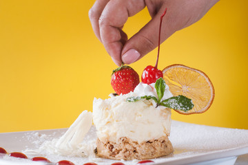 Decoration of creamy orange dessert by cherry. Delicious cake with dried citrus, white chocolate and mint on yellow background, real pleasure of sweets. Close up picture