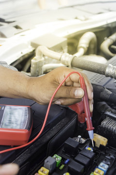 Auto mechanic uses a multimeter voltmeter to check the voltage level in a car battery.