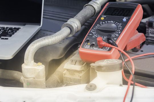 Auto mechanic uses a multimeter voltmeter to check the voltage level in a car battery.
