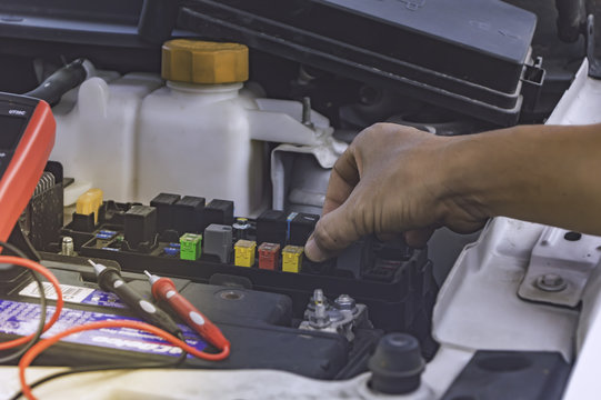 Auto mechanic uses a multimeter voltmeter to check the voltage level in a car batter.