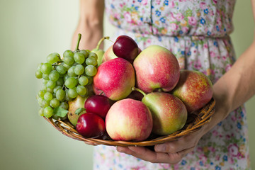 Female hands holding a wicker wooden plate with a harvest of autumn fruits. Harvest concept