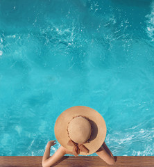 Back view of woman in straw hat relaxing in water swimming pool at luxury villa resort. Summer holiday idyllic background. Vacations Concept. Exotic Paradise.