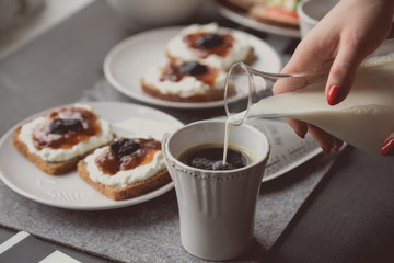 Breakfast with dark bread with white cheese and jam. Woman pouring milk for coffee