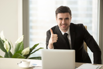 Successful confident businessman looking at camera, showing thumbs up or like sitting at office desk, effective solutions, recommending best choice for business, sign of success, good idea, great job