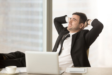 Happy relaxed businessman resting hands behind head near pc laptop looking away sitting at office desk with feet up on table, finished work, job done, completed all tasks, relaxing after hard workday