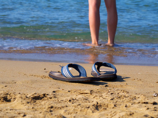 flippers on sand and man walking in water in background,