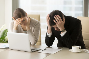 Tired frustrated business people feeling stressed, upset executives sitting near laptop, holding...