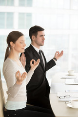 Relaxed mindful businessman and businesswoman meditating at work with eyes closed, chin mudra yogic...