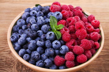 Blueberries and raspberries in clay bowl. Freshly picked berries on rustic background. Berry antioxidant superfood, concept for healthy eating