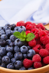 Blueberries and raspberries in clay bowl. Freshly picked berries on rustic background. Berry antioxidant superfood, concept for healthy eating