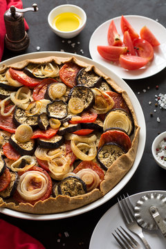 Homemade vegetable pie (galette) with grilled eggplants, tomatoes and onion on brown wooden background. Selective focus
