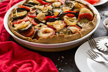 Homemade vegetable pie (galette) with grilled eggplants, tomatoes and onion on brown wooden background. Selective focus