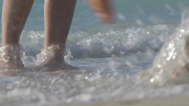 Beautiful female feet is walking on the beach. Legs washed by sea water. A lot of feet on the sandy beach. Waves flow down the legs. Fingernails in seawater. Slow motion