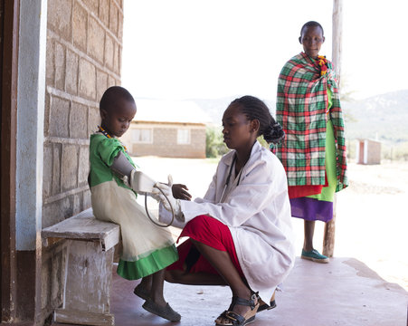 Female Doctor taking blood pressure of child (girl). Kenya, Africa.