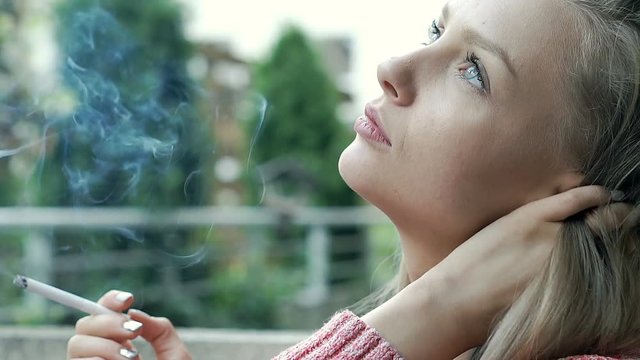 Pretty girl looks sad while sitting outdoors and smoking cigarette, steadycam shot

