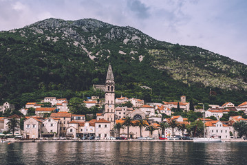 Perast, Montenegro - June 3th, 2016. View to famous coast village Perast Old Town roofs, promenade and mountains from water of Boka Kotorska. Postcard montenegrin landscape.