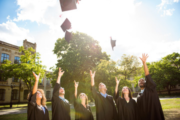 Six successful international young graduates in black robes and hats finished their education,...