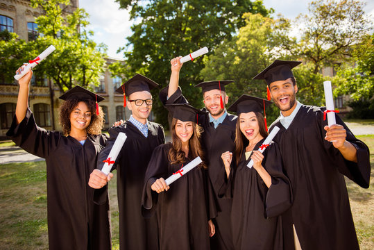 Triumph, education, graduation and people concept - group of happy six international students in mortar boards and bachelor gowns with diplomas,  celebrating success