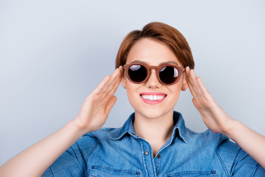Close up photo of funny smiling young woman in casual clothes touching her stylish sunglasses