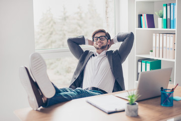 Portrait young relaxed handsome businessman with glasses is putting his feet on the desk in the office workstation and resting